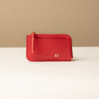 A red card case with a zipper coin compartment, made of polished pebble leather, with the letter 'D' visible on the front.