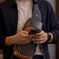 Man holding a black and brown Milano bag with a phone, wearing a dark jacket and white shirt.