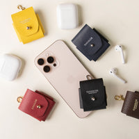 Several AirPod cases in different colors displayed alongside a smartphone and AirPods, with snap closures and ring attachments.