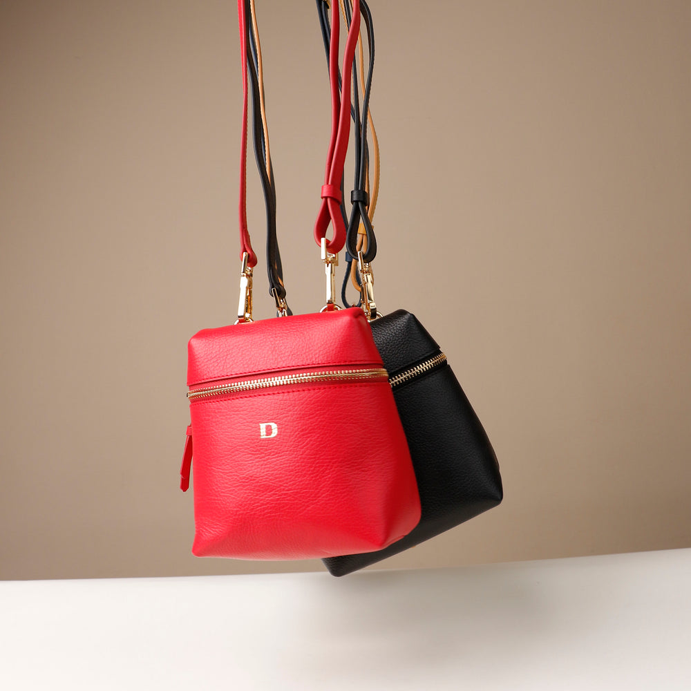 Red and black handbags with gold zippers on a beige background