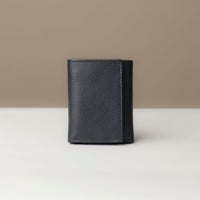 A closed trifold wallet in black color, made from pebbled leather, displayed against a neutral background.
