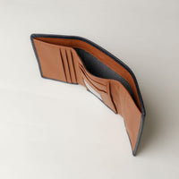A open trifold wallet in black and tan color, made from pebbled leather with nappa leather interior, with 6 slots for cards and a long comparment for cash, displayed against a neutral background. Upper view. 