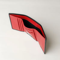 A open trifold wallet in black and red color, made from pebbled leather with nappa leather interior, with 6 slots for cards and a long comparment for cash, displayed against a neutral background. Upper view. 