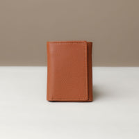 A pebble tan trifold wallet made of pebble leather, closed and viewed from the front against a neutral background.