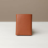 A closed pebble tan trifold wallet made of pebble leather viewed from the front against a neutral background. 