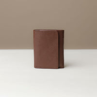 A brown trifold wallet made of pebble leather, closed and viewed from the front on a light background.