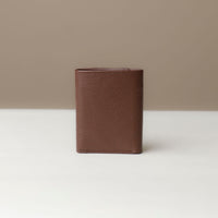 Another view of a brown trifold wallet made of pebble leather, closed and viewed from the front on a light background.