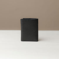 Another view of a closed trifold wallet in black color, made from pebbled leather, displayed against a neutral background.