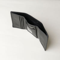 A open trifold wallet in black color, made from pebbled leather, with nappa leather slots for cards, displayed against a neutral background. Upper view. 