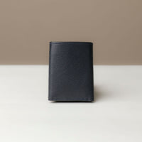 A trifold wallet in black color, made from pebbled leather, displayed against a neutral background. Closed view.