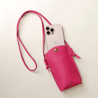 Pink crossbody bag with a phone inside on a light beige background