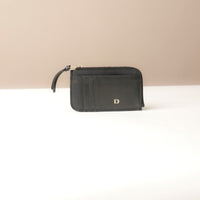 Black card case wallet with a gold zipper and brand logo on a beige background