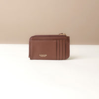 Brown card case wallet with gold zipper on a beige background