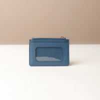 back view of a pebble leather card case nirua in navy blue with gold accents over a beige background