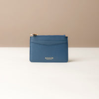 front view of a pebble leather card case nirua in navy blue with gold accents over a beige background