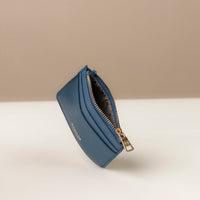 upper view of a open pebble leather card case nirua in navy blue with gold accents over a beige background
