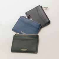 three pebble leather card case nirua in dark green, blue and black with gold accents over a beige background