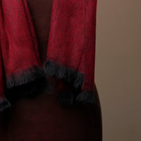 Red scarf with black fringe draped over a person against a brown background