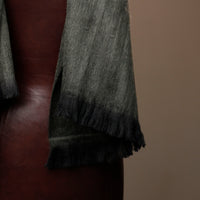 Gray scarf with fringes draped over a brown leather surface against a beige background