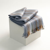 Striped blanket draped over a white cube on a light gray background