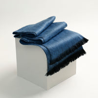 Folded blue denim blanket on a white block with a white background