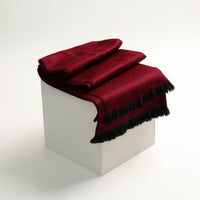 Red blanket with black fringe draped over a white cube on a white background