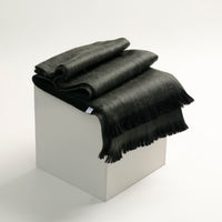 Black blanket with fringes on a white box against a white background