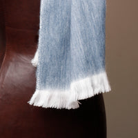 Light blue scarf with white fringe on a brown leather surface