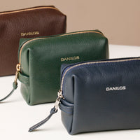 Leather toiletry bags in brown, green, and navy colors, displayed against a neutral background.