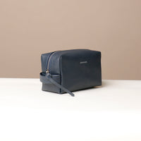 Leather toiletry bags in brown, green, and navy colors, displayed against a neutral background.