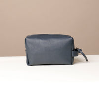 Leather toiletry bags in brown, green, and navy colors, displayed against a neutral background.