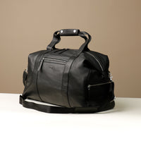 Angled View of a black leather duffle bag with zippered compartment on the front side and double handle.