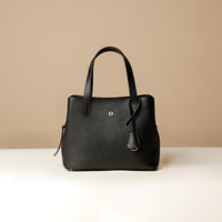 A black leather top handle bag with a zipper closure and a detachable strap, placed against a beige background.