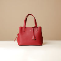 A red leather top handle bag with a zipper closure and a detachable strap, placed against a beige background.