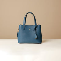 A blue leather top handle bag with a zipper closure and a detachable strap, placed against a beige background.