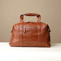 A brown leather duffle bag with zippered compartment on the front side.