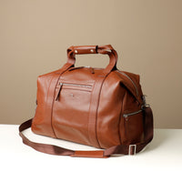 Angled View of A brown leather duffle bag with zippered compartment on the front side and double handle.