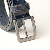 Close up view of A blue double stitch belt with a metallic buckle on a light background.
