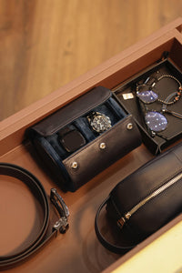 Open jewelry box with watch, sunglasses, and belt on a wooden surface