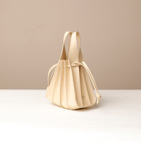 A beige, mini bucket-style leather handbag with pleated details and a drawstring closure, displayed against a neutral background.