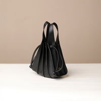 A black, mini bucket-style leather handbag with pleated details and a drawstring closure, displayed against a neutral background.