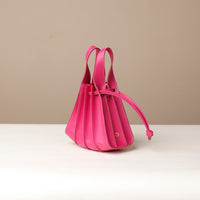 A Pink, mini bucket-style leather handbag with pleated details and a drawstring closure, displayed against a neutral background.