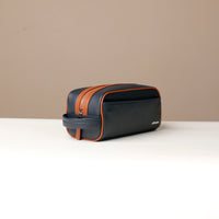 A pebble blue and tan Emmiliano toiletry bag with zipper closure, with brand Danilos, placed against a neutral background. Lateral view. 