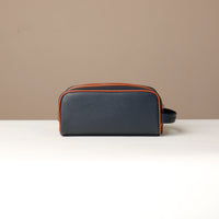 A pebble blue and tan Emmiliano toiletry bag with zipper closure, placed against a neutral background. Back view. 
