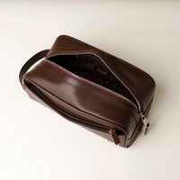 A pebble brown, full-grain leather toiletry bag Emmiliano with a zipper closure, displayed against a neutral background. Open view. 