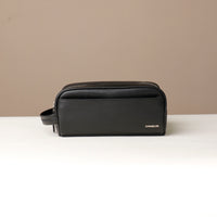 A pebble black, full-grain leather Emmiliano toiletry bag with a zipper closure, displayed against a neutral background. Front view. 
