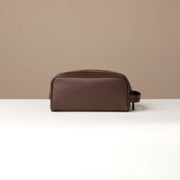 A pebble brown, full-grain leather toiletry bag Emmiliano with a zipper closure, displayed against a neutral background. Back view. 