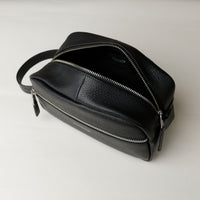 A open black toiletry bag 2014 with a silver zipper closure and a handle, with visible brand Danilos, placed against a neutral background. Upper view. 