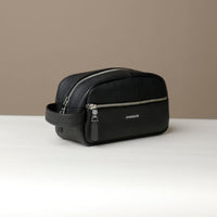 A black toiletry bag 2014 with a silver zipper closure and a handle, with visible brand Danilos, placed against a neutral background. Lateral view. 