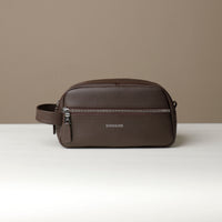 A brown toiletry bag 2014 with a silver zipper closure and a handle, with visible brand Danilos, placed against a neutral background. Front view. 